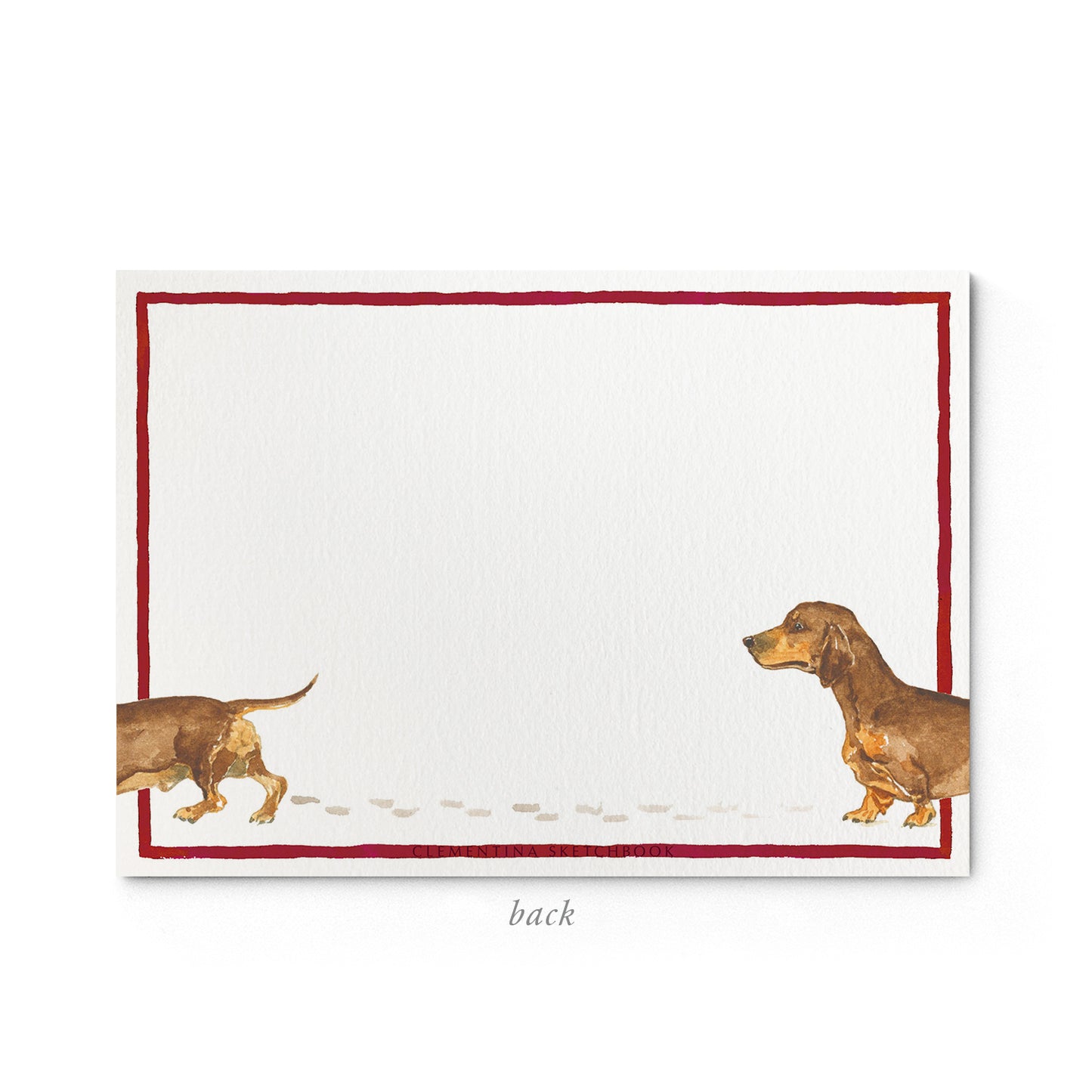 Image shows the back of a Clementina Sketchbook sausage dog stationery card, with a daschund watercolour design and a dark red border.