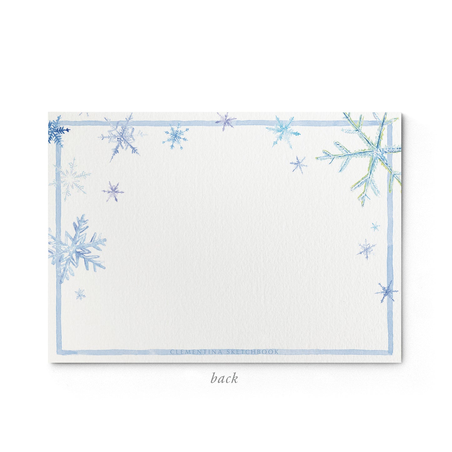 Image shows the back of a Clementina Sketchbook Christmas stationery card, with a snowflake watercolour design and a light blue border.