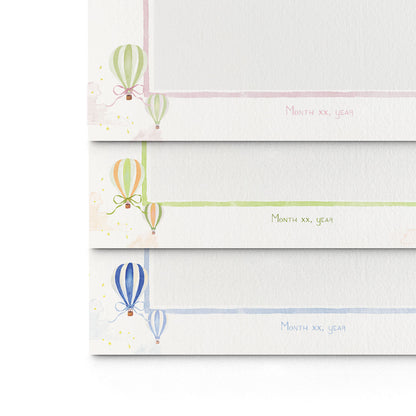 Close-up of the three different variations of Clementina Sketchbook's hot air balloon printed birth announcements layered on top of each other, showcasing the watercolour designs.