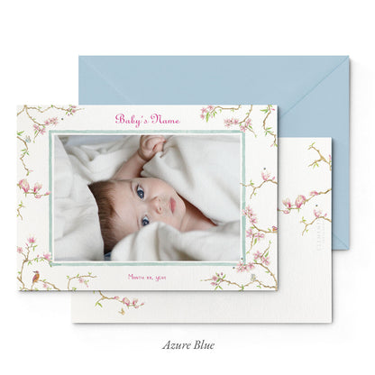 Image of both sides of Clementina Sketchbook's magnolia printed birth announcement with a floral border, personalised text, space for a baby photo to be stuck and a blue envelope.